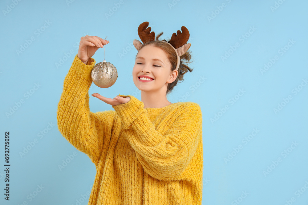 Young woman in reindeer horns with Christmas ball on blue background