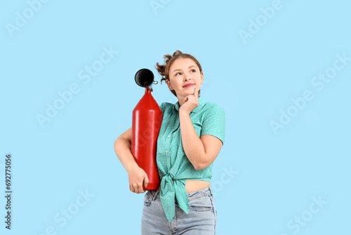 Thoughtful young woman with fire extinguisher on blue background photo