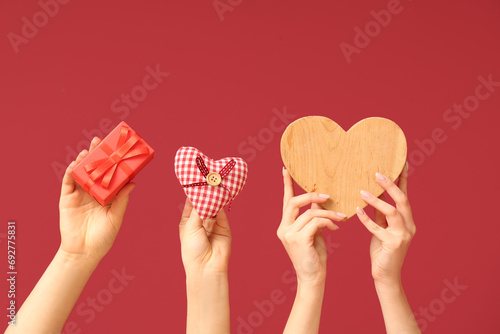 Slika na platnu Female hands with gift box, wooden and fabric hearts on red background