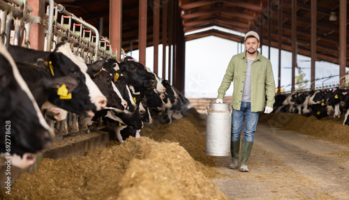 Male farmer carries a large milk can in his hands at a cow farm photo