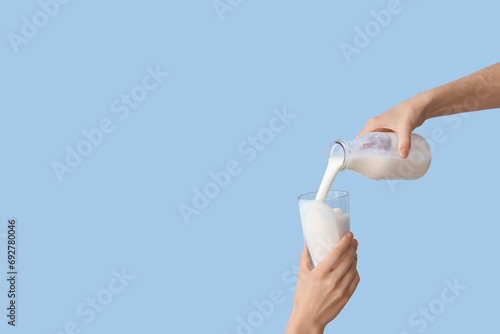Hands pouring milk from bottle into glass on light blue background photo