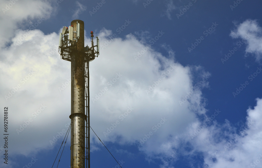 High metal chimney of industrial plant with ladder in the form of metal braces against the background of a cloudy blue sky High metal chimney of industrial plant with ladder in the form of metal braces against the background of a cloudy blue sky