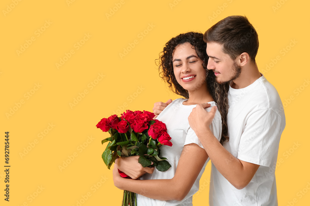 Young couple with rose flowers for Valentine's day on yellow background