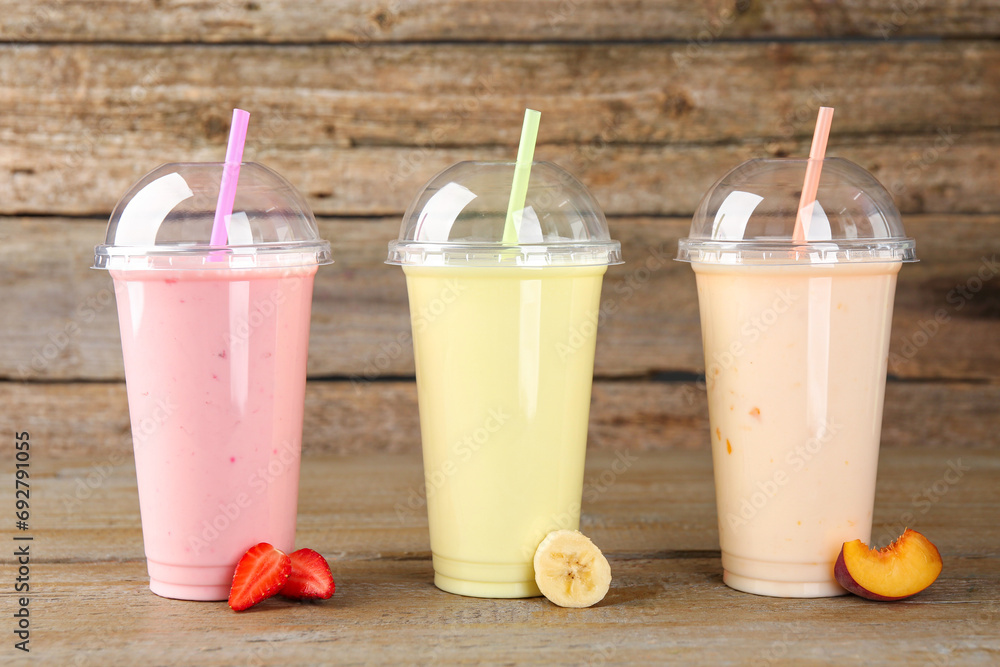 Plastic cups with different tasty smoothies and fresh fruits on wooden table Plastic cups with different tasty smoothies and fresh fruits on wooden table