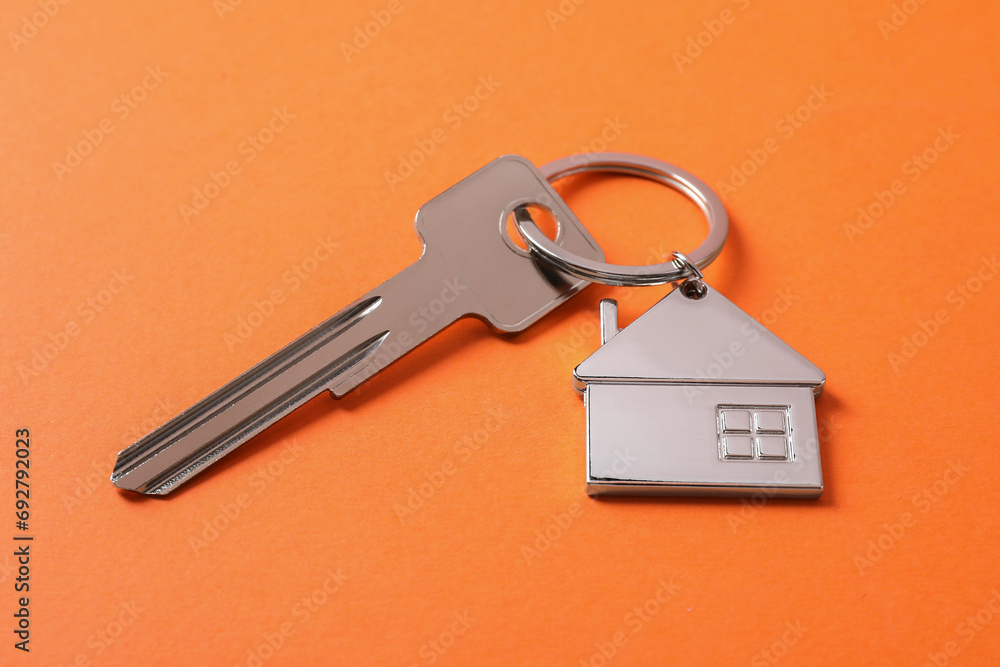 Metallic key with keychain in shape of house on orange background Metallic key with keychain in shape of house on orange background
