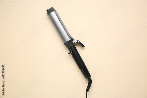 Hair curling iron on beige background, top view
