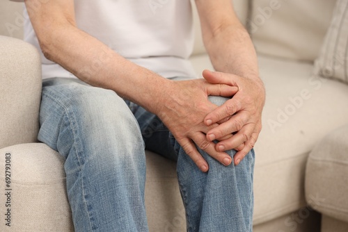 Senior man suffering from knee pain on sofa, closeup. Rheumatism symptom