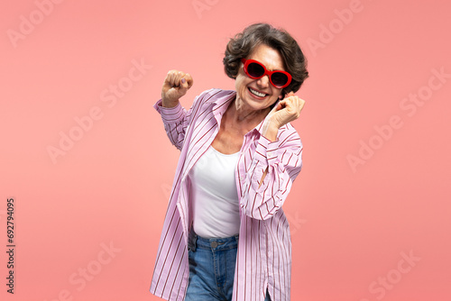 Smiling senior woman, happy funny grandmother wearing stylish pink shirt dancing, having fun isolated on background 
