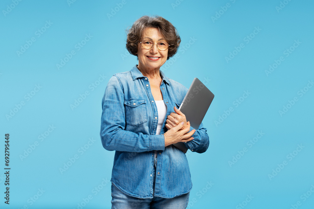 Beautiful attractive senior business woman, happy modern grandmother holding laptop computer looking at camera isolated on blue background. Successful business Beautiful attractive senior business woman, happy modern grandmother holding laptop computer looking at camera isolated on blue background. Successful business