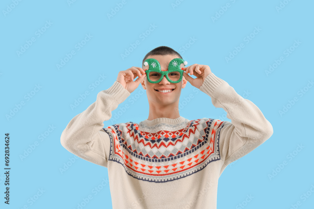 Teenage boy in Christmas eyeglasses on blue background Teenage boy in Christmas eyeglasses on blue background