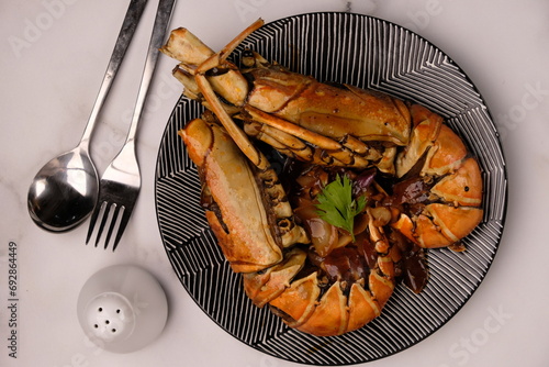 Lobster saus lada hitam or Lobster in black pepper sauce. Served on a ceramic plate on marble table.  Stainless steel cutlery. Indonesian food. photo