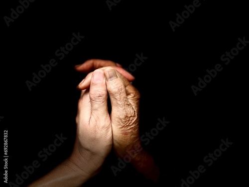 The hands of an old mother and her daughter are hold together at the tips of the fingers.