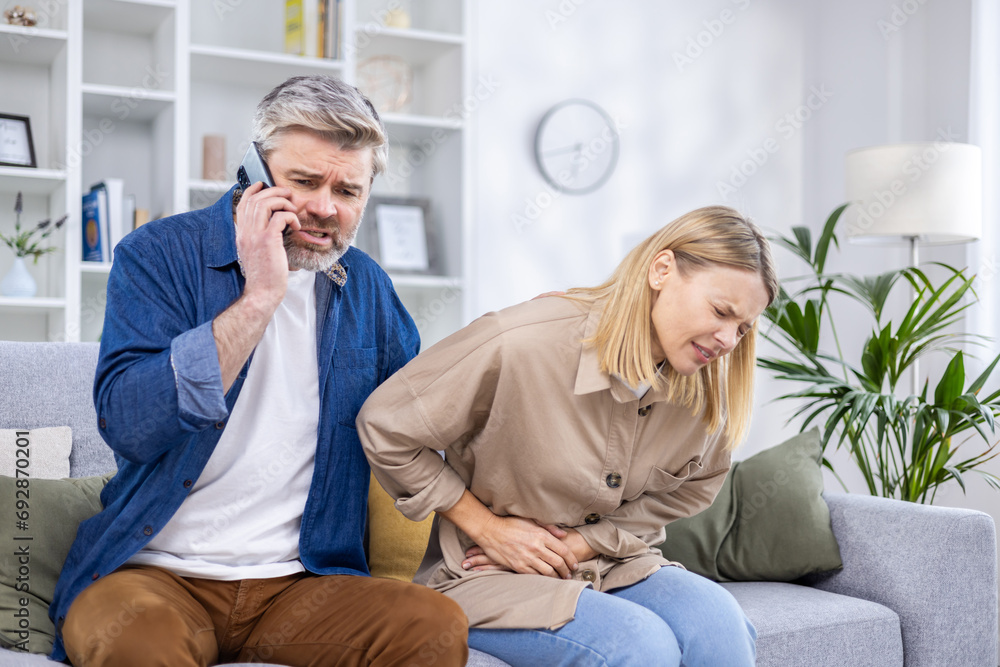 Worried husband calls an ambulance for his wife who has a stomach ache, husband calls on the phone while sitting on the sofa. Worried husband calls an ambulance for his wife who has a stomach ache, husband calls on the phone while sitting on the sofa.