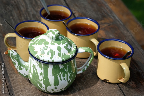 Teh Poci Gula Batu, Teko Blirik. is hot tea sweetened with rock sugar, served with an antique enamel teapot and an enemel cup on the brown wooden rustic table. Indonesian Drinks.  photo