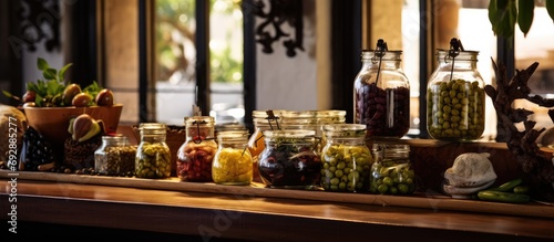 In the restaurant, there's a wooden counter with a basket of fruit and plates, as well as a shelf displaying glass jars of olives.