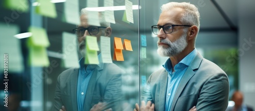 In a corporate office, a senior businessman leads a strategy meeting, encouraging creative thinking and brainstorming with sticky notes on a glass wall.