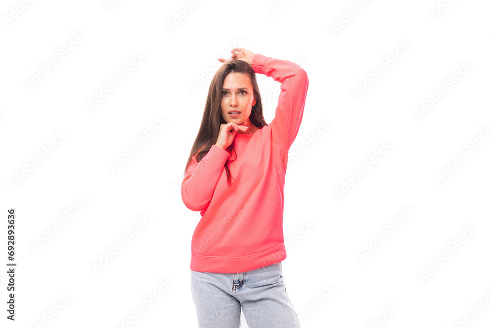 pretty young brunette caucasian woman with straight hair is dressed in a pink sweatshirt and jeans on a white background with copy space pretty young brunette caucasian woman with straight hair is dressed in a pink sweatshirt and jeans on a white background with copy space
