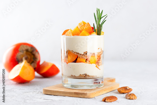 Trifle with persimmon, rosemary, pecan, whipped coconut cream and biscuit on a wooden board. Healthy food, vegan, sugar, gluten and lactose free.