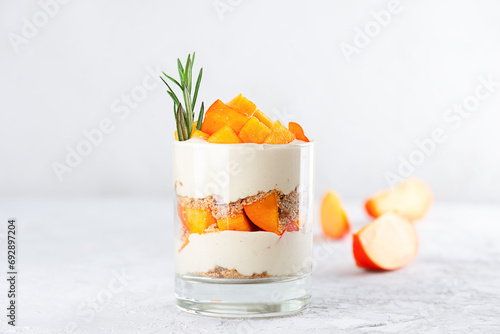Dessert in a glass with persimmon, rosemary, pecan, whipped coconut cream. Healthy food, vegan, sugar, gluten and lactose free. photo