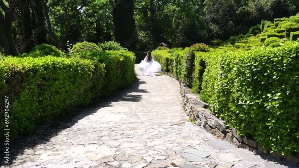 Happy Woman run in the park among lush green bushes, slow-motion. Girl in white flying dress with long Blond hair in the garden. Slim lady's outdoor Springtime joy Happy Woman run in the park among lush green bushes, slow-motion. Girl in white flying dress with long Blond hair in the garden. Slim lady's outdoor Springtime joy