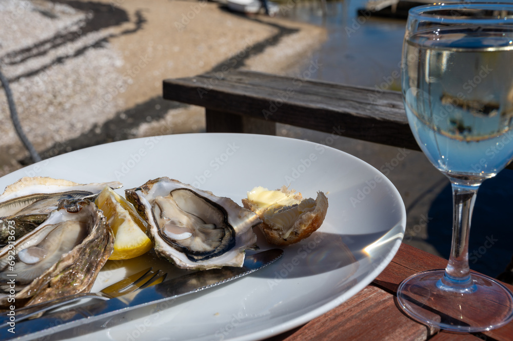 Eating of fresh live oysters with glass of white wine at farm cafe in oyster-farming village, with view on boats and water of Arcachon bay, Cap Ferret peninsula, Bordeaux, France