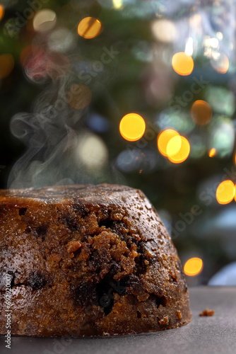 Close up shot of a steaming, hot Christmas pudding infront of Christmas lights.