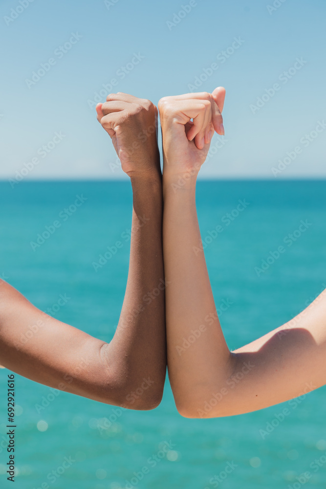 Crop faceless diverse girlfriends bumping elbows at seaside Crop faceless diverse girlfriends bumping elbows at seaside