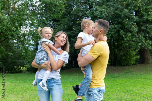 A young family in jeans and white T-shirts plays with small children in a green summer park on a sunny day.