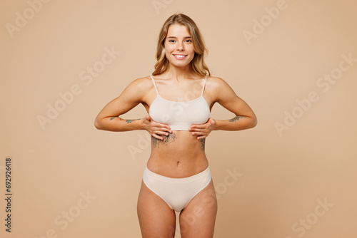 Young nice lady woman with slim body perfect skin wear nude top bra lingerie stand put hand on chest cancer early diagnostic isolated on plain pastel light beige background Lifestyle diet fit concept