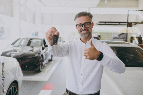 Adult man customer male buyer client wear shirt hold car keys fob keyless system show thumb up choose auto want buy new automobile in showroom vehicle salon dealership store motor show. Sales concept. © ViDi Studio