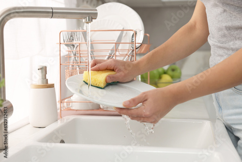 Woman washing plate at sink in kitchen, closeup photo