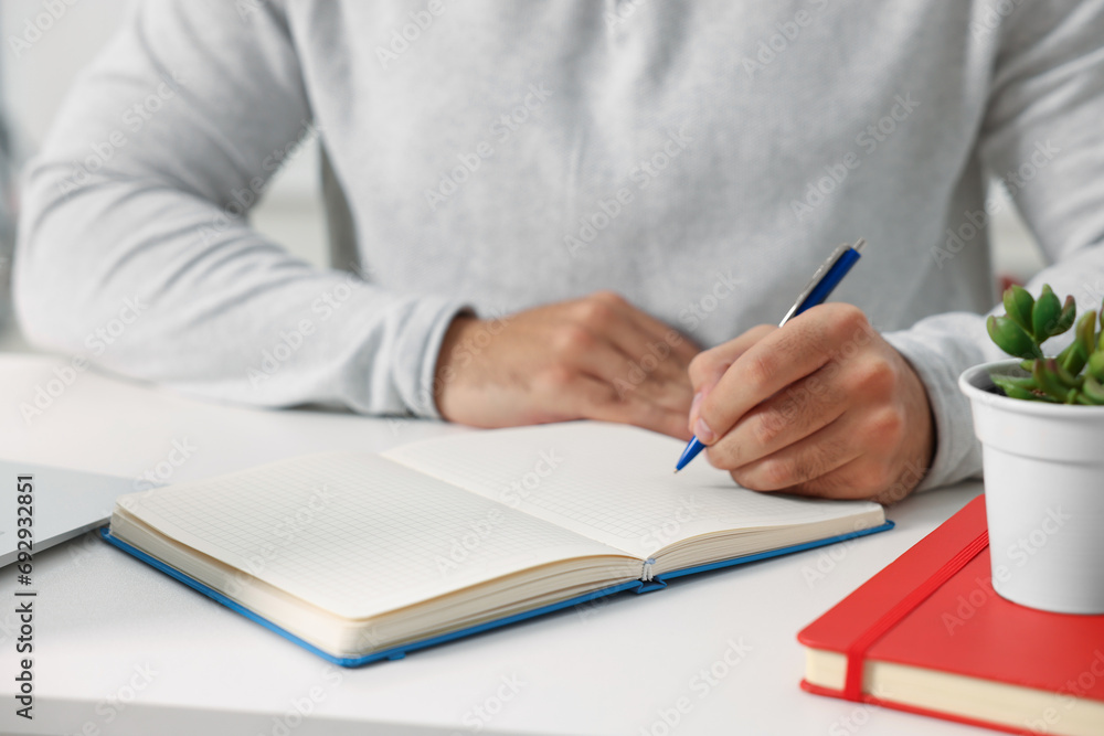 Young man writing in notebook at white table, closeup Young man writing in notebook at white table, closeup