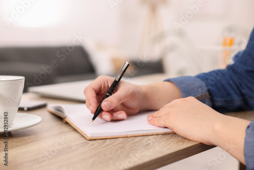 Young woman writing in notebook at wooden table, closeup photo