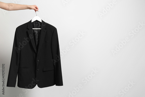 Fotografi Woman holding hanger with black jacket near white wall, closeup