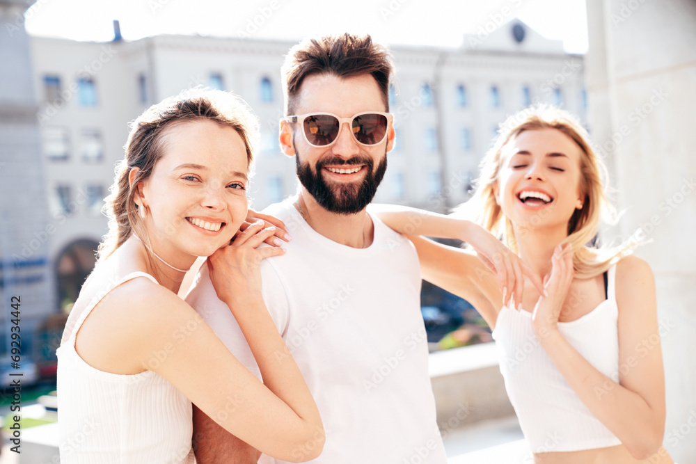 Group of young three stylish friends posing in the street. Fashion man and two cute female dressed in casual summer clothes. Smiling models having fun. Cheerful women and guy outdoors at sunny day Group of young three stylish friends posing in the street. Fashion man and two cute female dressed in casual summer clothes. Smiling models having fun. Cheerful women and guy outdoors at sunny day