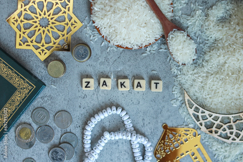 Top view of wooden blocks with Zakat word, rice grain on bowl, rosary beads, money coins.  Islamic zakat concept  photo