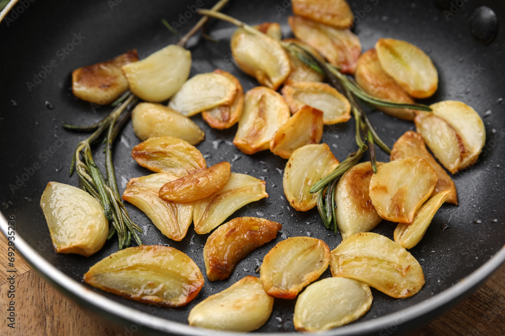 Frying pan with fried garlic cloves and rosemary, closeup Frying pan with fried garlic cloves and rosemary, closeup