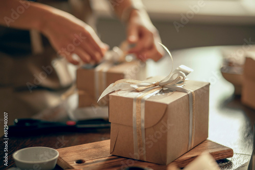 A craft box with white and gold ribbons. A woman's hands ties a ribbon on a customer's order box. A small business entrepreneur and the concept of food delivery.