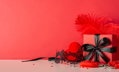 Romantic surprise awaits in discreet gift box adorned with sleek black bow. Explore pleasure with adult toys, furry handcuffs, feather tickler, and sprinkles. Side view photo, red background sets mood