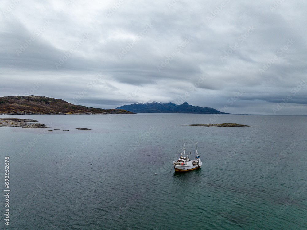 aerial view from drone of a small fisherman boat next to a rocky shore of norwegian sea with cyan blue water