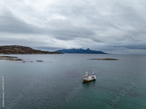 aerial view from drone of a small fisherman boat next to a rocky shore of norwegian sea with cyan blue water © Sid Smith