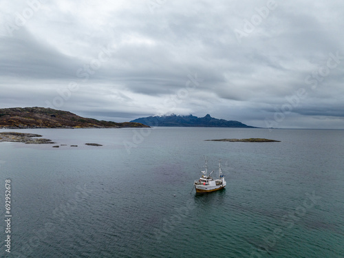 Obraz na płótnie aerial view from drone of a small fisherman boat next to a rocky shore of norwegian sea with cyan blue water w salonie