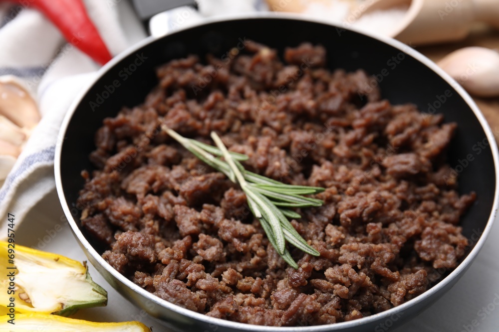 Fried ground meat in frying pan and rosemary on white table, closeup Fried ground meat in frying pan and rosemary on white table, closeup