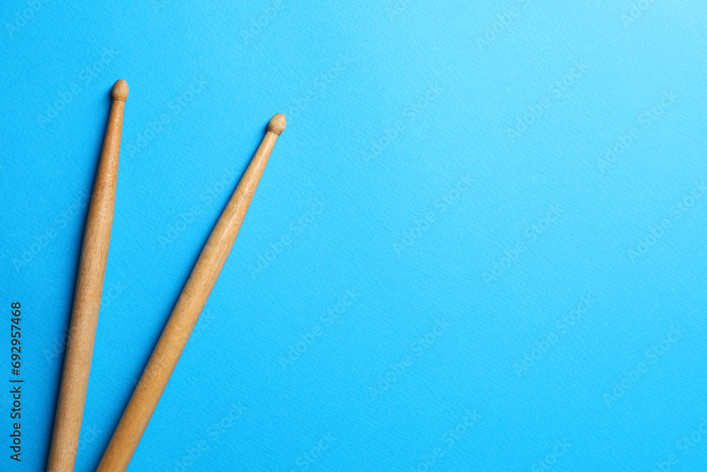 Two wooden drum sticks on light blue background, top view. Space for text Two wooden drum sticks on light blue background, top view. Space for text