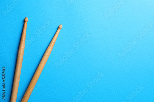 Two wooden drum sticks on light blue background, top view. Space for text