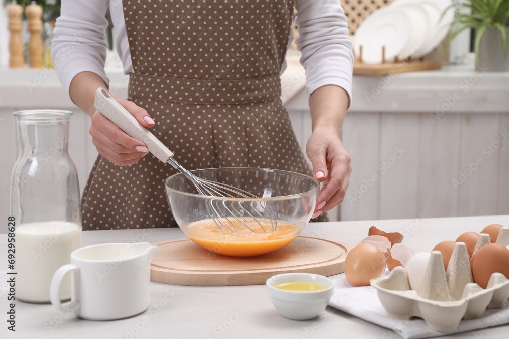 Woman whisking eggs in bowl at table indoors, closeup Woman whisking eggs in bowl at table indoors, closeup