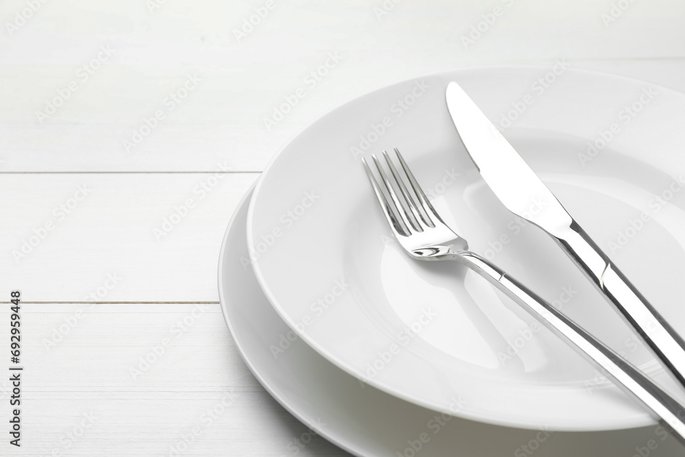 Clean plates, fork and knife on white wooden table, closeup. Space for text Clean plates, fork and knife on white wooden table, closeup. Space for text