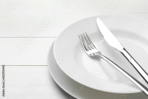 Clean plates  fork and knife on white wooden table  closeup. Space for text