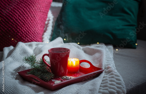 red cup of tea on wooden tray with fir branches on sofa