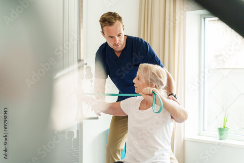 Senior woman performing arm-strengthening exercises with resistance band under the guidance of a professional physiotherapist.